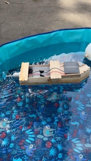 Barco com casco de palitos, motor e painel solar flutuando em uma piscina