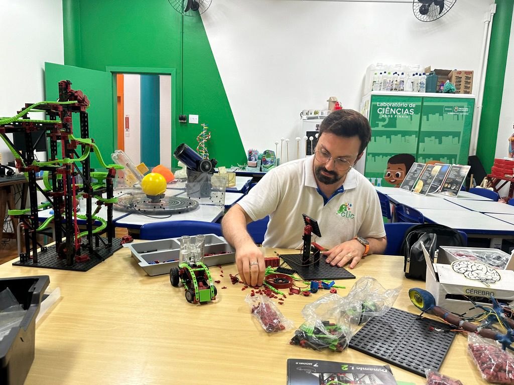 Professor Fábio Fialho Meneghesso montando um modelo com peças de encaixe, ao lado de outras construções de robótica sobre a mesa do laboratório
