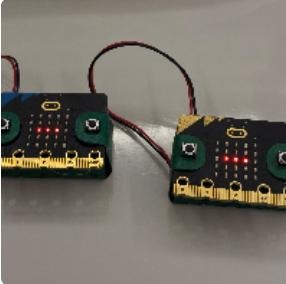 Duas placas micro:bit lado a lado, com LEDs acesos, ligadas por fios a pilhas